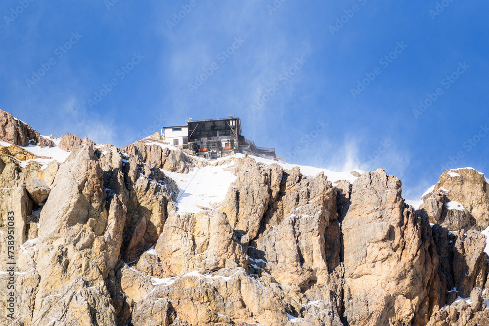 Fototapeta premium Low angle view of a cable car top station on snow covered rocky mountain peak on a windy winter day
