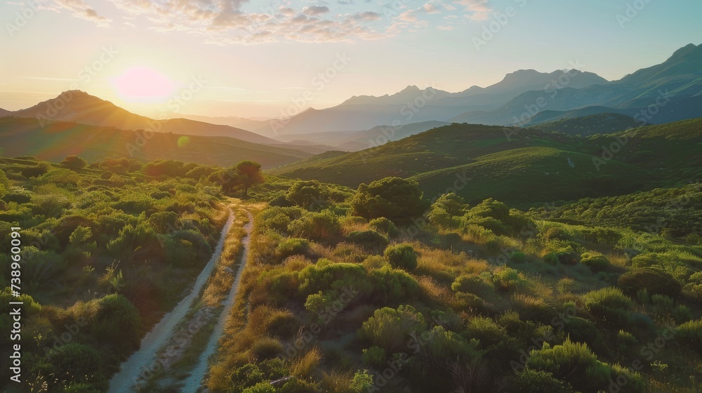Embracing the beauty of nature, a winding dirt road leads through a lush green valley, surrounded by majestic mountains and vibrant plant life as the sun rises over the horizon, casting a golden glow