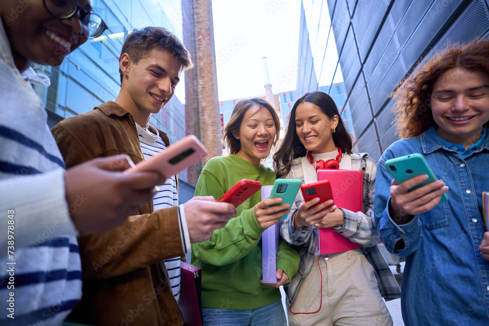 Obraz premium Group of young people in circle using cell phones together outdoor. Cheerful friends meeting looking at colorful mobiles enjoying fun content on social networks. Generation z, addiction to technology