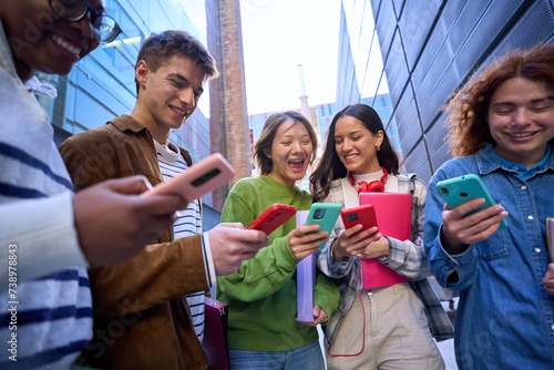 Group of young people in circle using cell phones together outdoor. Cheerful friends meeting looking at colorful mobiles enjoying fun content on social networks. Generation z, addiction to technology photo