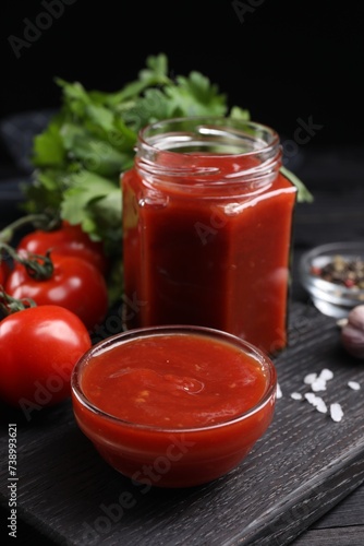 Delicious ketchup and products on black wooden table, closeup. Tomato sauce