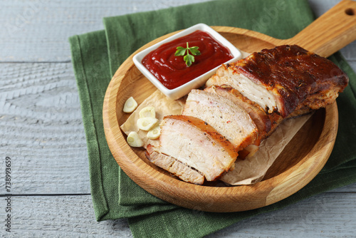 Pieces of baked pork belly served with sauce on grey wooden table