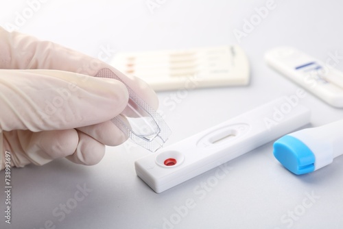 Doctor dropping buffer solution onto disposable express test cassette on light background, closeup