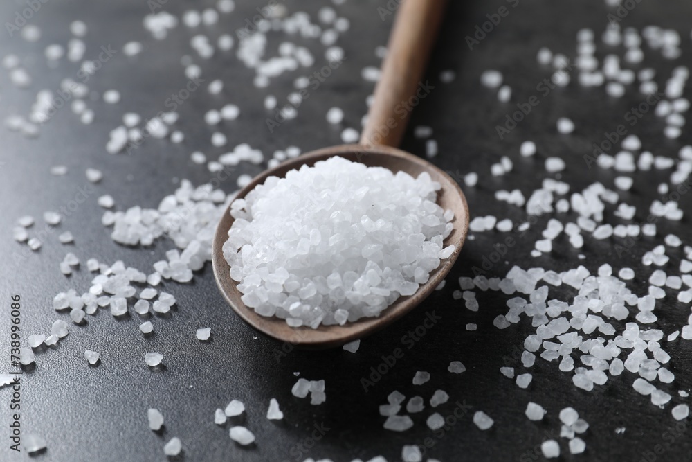 Natural salt and wooden spoon on black table, closeup Natural salt and wooden spoon on black table, closeup