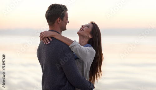 Love  hug and happy couple at ocean at sunset for tropical holiday adventure  relax and bonding together. Laughing  man and woman on romantic date with beach  evening sky and embrace on vacation.