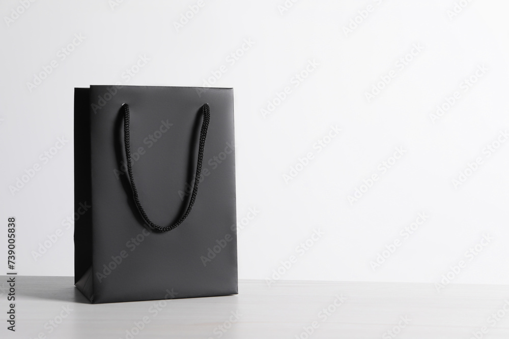 Black paper bag on white wooden table, space for text Black paper bag on white wooden table, space for text