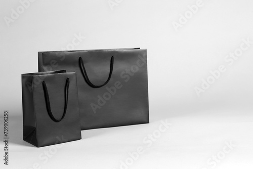 Two black paper shopping bags on grey background. Space for text