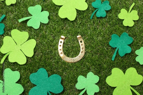 St. Patrick's day. Golden horseshoe surrounded by felt clover leaves on green grass, flat lay