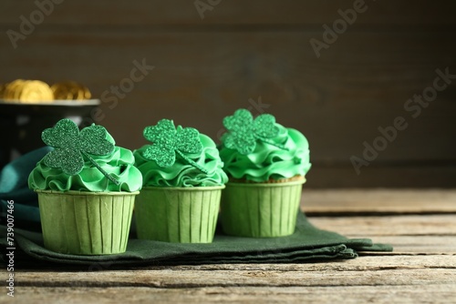 Fototapeta Naklejka Na Ścianę i Meble -  St. Patrick's day party. Tasty cupcakes with clover leaf toppers and green cream on wooden table, closeup. Space for text