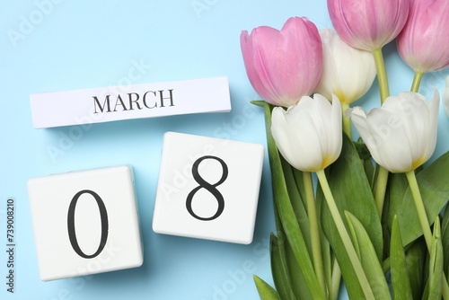 International Women's day - 8th of March. Wooden block calendar and beautiful flowers on light blue background, flat lay