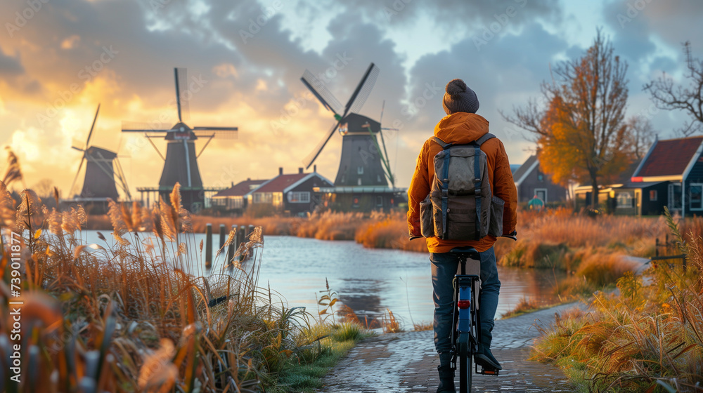 dutch windmill in the country with a man on a bicycle - obrazy, fototapety, plakaty 