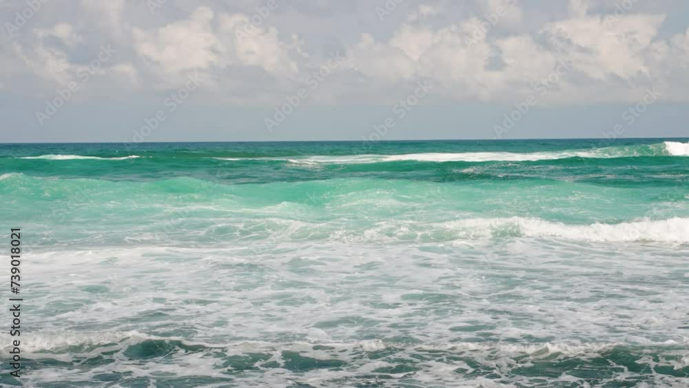 Turquoise waves crash onto shore under blue sky. White foam spreads on beach. Clear water sparkles in sunlight. Peaceful ocean scene for relaxation and nature themes. Waves roll in continuous loop. Turquoise waves crash onto shore under blue sky. White foam spreads on beach. Clear water sparkles in sunlight. Peaceful ocean scene for relaxation and nature themes. Waves roll in continuous loop.