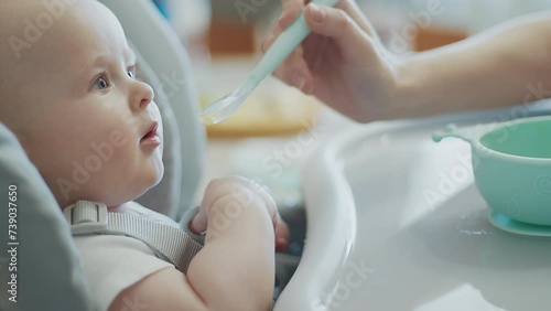 Feed time for cute baby with open mouth, anticipation, highchair seat, mother interaction, mealtime bonding. Infant experience first time feeding, expressive meal moment, caregiver hand with spoon. photo