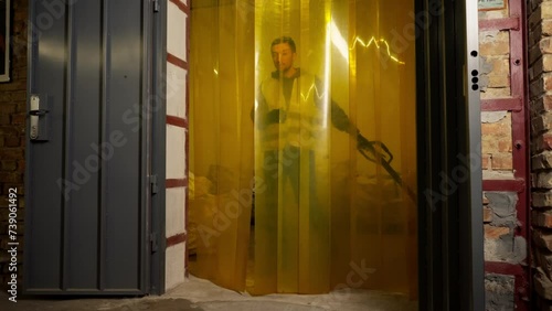 A worker at a waste processing plant in a work vest passes through a silicone curtain at the door of a waste sorting plant photo