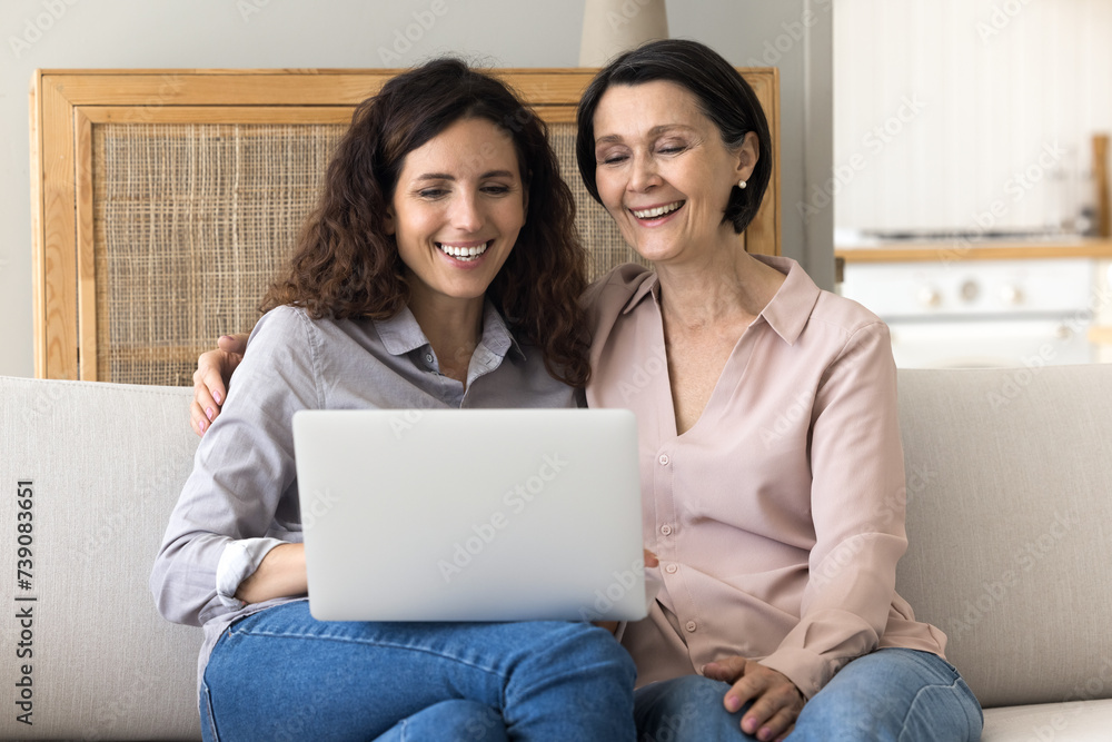 Cheerful mother her millennial daughter spend free time together resting on sofa with laptop, watch comedy movie, enjoy videos, buy online. Modern tech usage, subscription services for fun and leisure Cheerful mother her millennial daughter spend free time together resting on sofa with laptop, watch comedy movie, enjoy videos, buy online. Modern tech usage, subscription services for fun and leisure