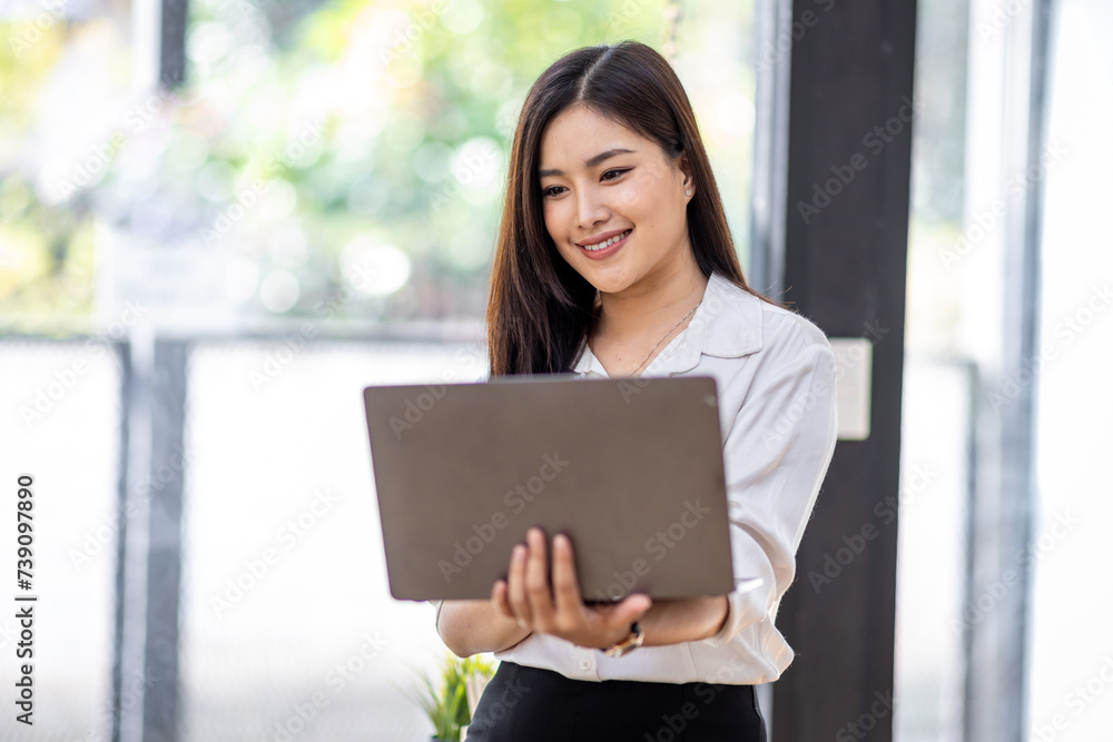 Portrait of Asian beautiful joyful woman holding laptop doing finance and standing in the office