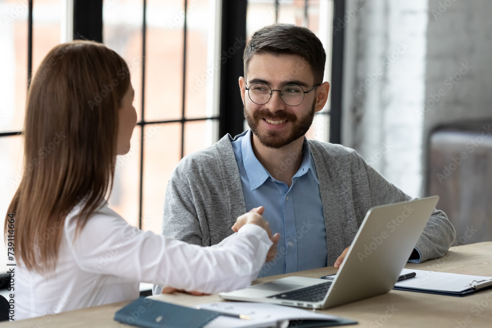 Obraz premium Female client shaking hands with male loan officer. Customer thanking friendly bank worker for financial advice. Happy young entrepreneurs making a deal. CEO welcoming new employee to modern company