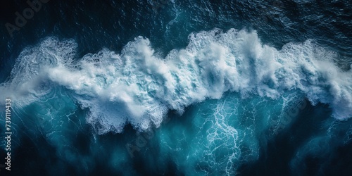 A powerful surging wave of the sea is depicted in this breathtaking aerial image as it crashes into a frothy foam against the dark depths below  evoking a sense of wonder and strength.