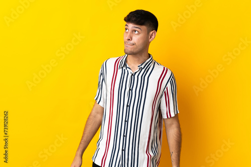 Young Colombian man isolated on yellow background having doubts while looking up