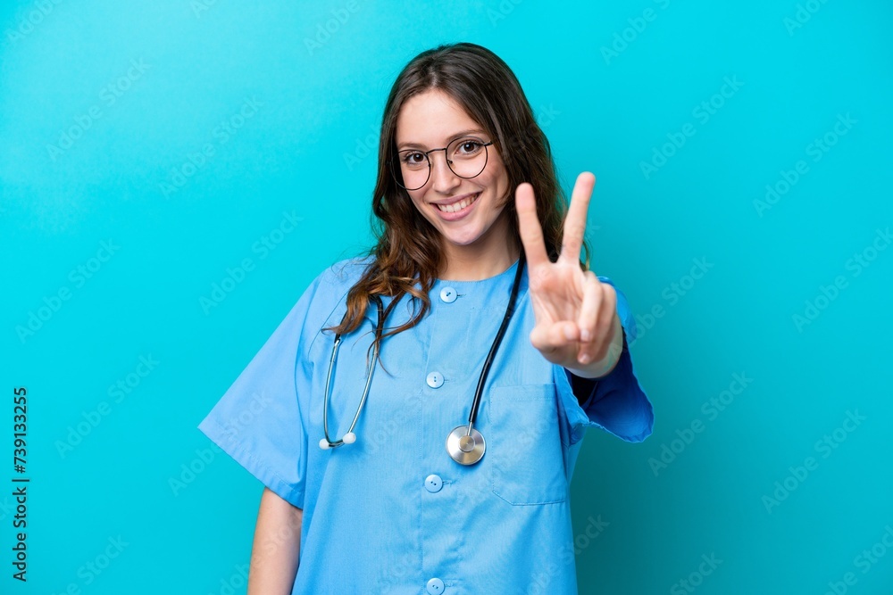 © luismolinero - Young surgeon doctor woman isolated on blue background smiling and showing victory sign