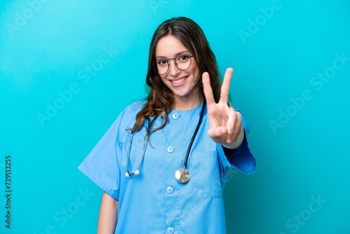 Young surgeon doctor woman isolated on blue background smiling and showing victory sign