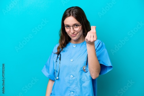 Young surgeon doctor woman isolated on blue background making money gesture