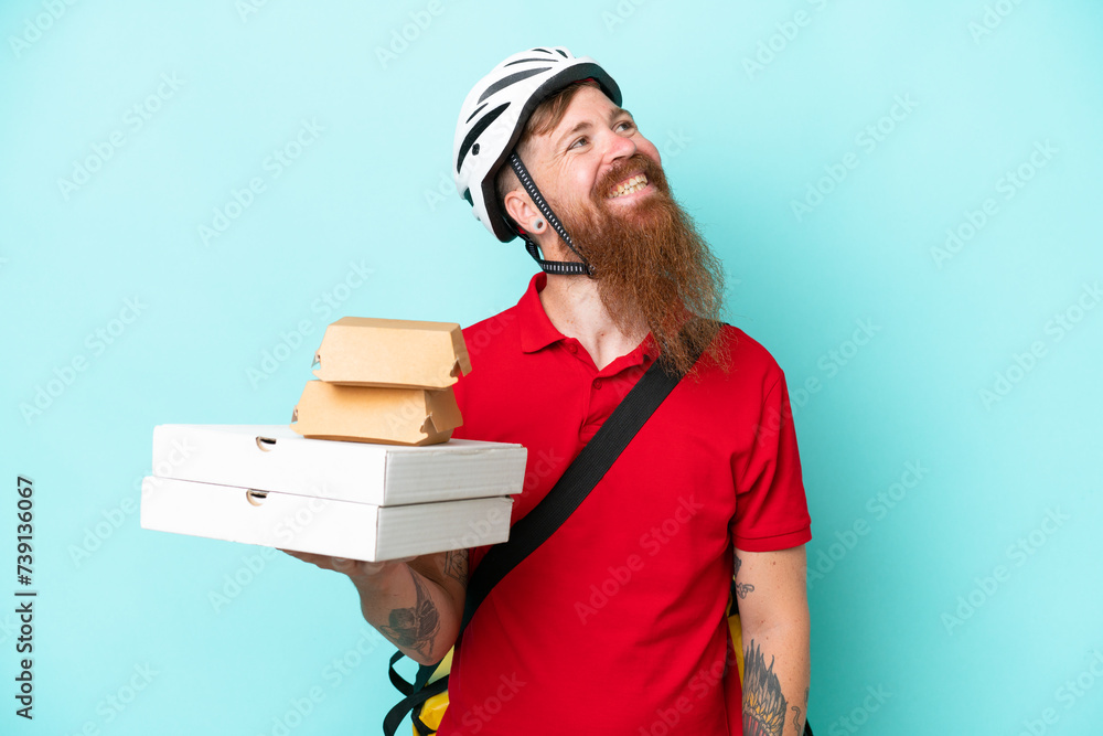 Delivery man holding pizzas and burgers isolated on blue background thinking an idea while looking up Delivery man holding pizzas and burgers isolated on blue background thinking an idea while looking up