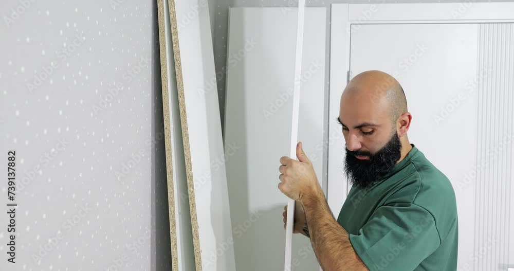 Side view. The process of assembling a wardrobe on your own at home in the children's room. The bearded dad takes out a part for the closet door from the box and leans against the wall. Side view. The process of assembling a wardrobe on your own at home in the children's room. The bearded dad takes out a part for the closet door from the box and leans against the wall.