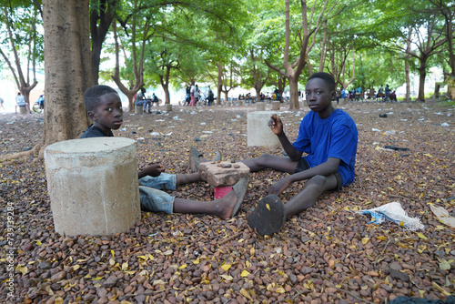 Two small black West African boys sitting in a public park busy playing tic tac toe with little stones on a makeshift game board