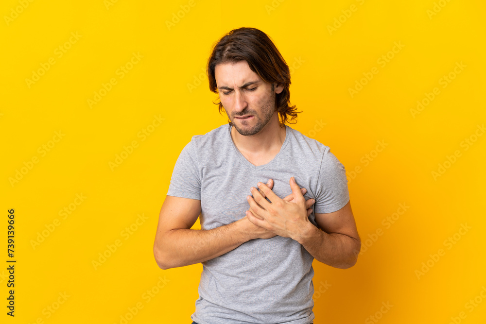 Young handsome man isolated on yellow background having a pain in the heart Young handsome man isolated on yellow background having a pain in the heart