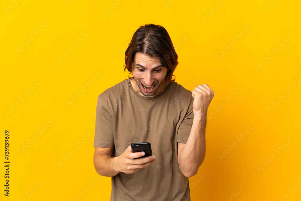 Young handsome man isolated on yellow background surprised and sending a message Young handsome man isolated on yellow background surprised and sending a message