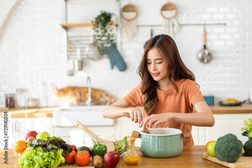 Young woman standing near stove and cooking, housewife, meal, chef, food.Happy woman looking and smelling tasting fresh delicious from soup in a pot with steam at white interior kitchen