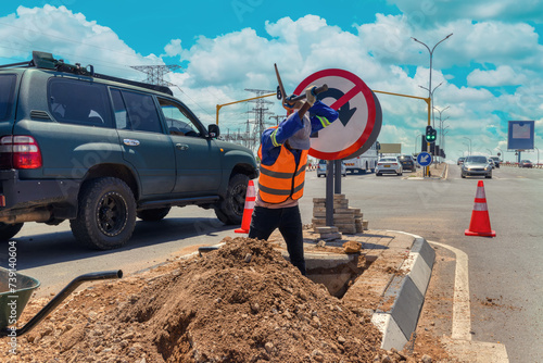 african american worker with a pickaxe digging a ditch in the highway to repair cabling on an isle at an intersection