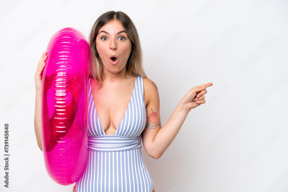 Young Rumanian woman in swimsuit holding a air mattress donut isolated on white background surprised and pointing side Young Rumanian woman in swimsuit holding a air mattress donut isolated on white background surprised and pointing side