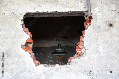 Large hole in an old brick wall. There's a lantern hanging behind the wall