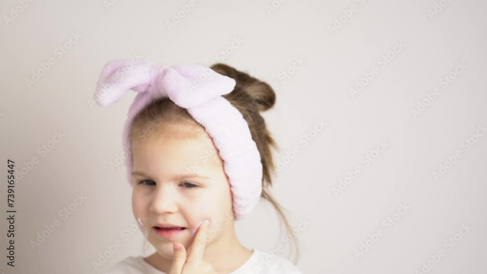 Funny happy attractive little girl in lavender headband apply skincare cream on face, toddler girl put moisturizer or sunscreen facial cream, skin care treatment, atopic skin concept Funny happy attractive little girl in lavender headband apply skincare cream on face, toddler girl put moisturizer or sunscreen facial cream, skin care treatment, atopic skin concept