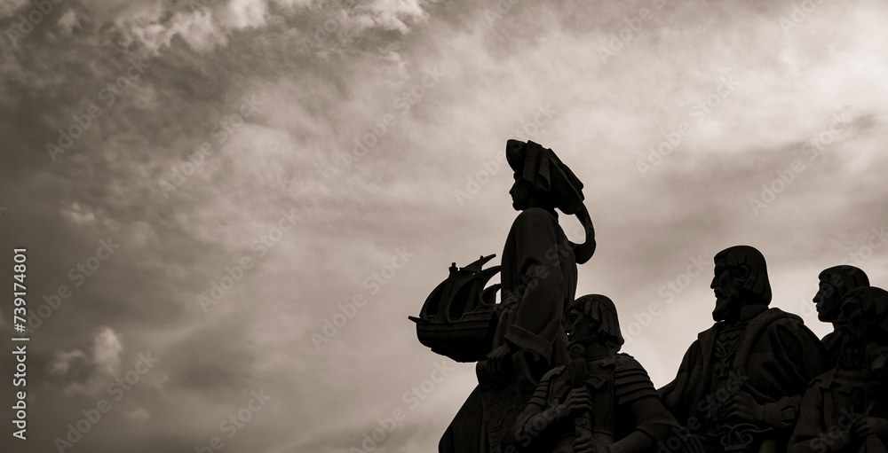Backlit silhouettes of limestone sculptures and Henry the Navigator holding in his hand a ship from the Monument to the Discoveries in Lisbon with a spectacular dramatic cloudy sky at sunset. Backlit silhouettes of limestone sculptures and Henry the Navigator holding in his hand a ship from the Monument to the Discoveries in Lisbon with a spectacular dramatic cloudy sky at sunset.