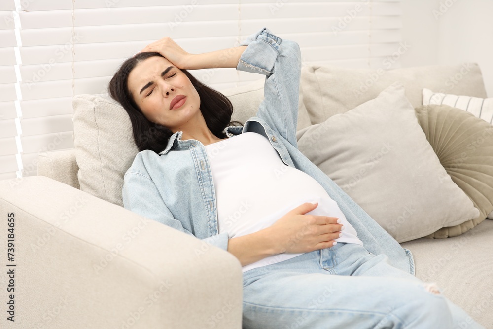 Pregnant woman suffering from headache on sofa at home Pregnant woman suffering from headache on sofa at home