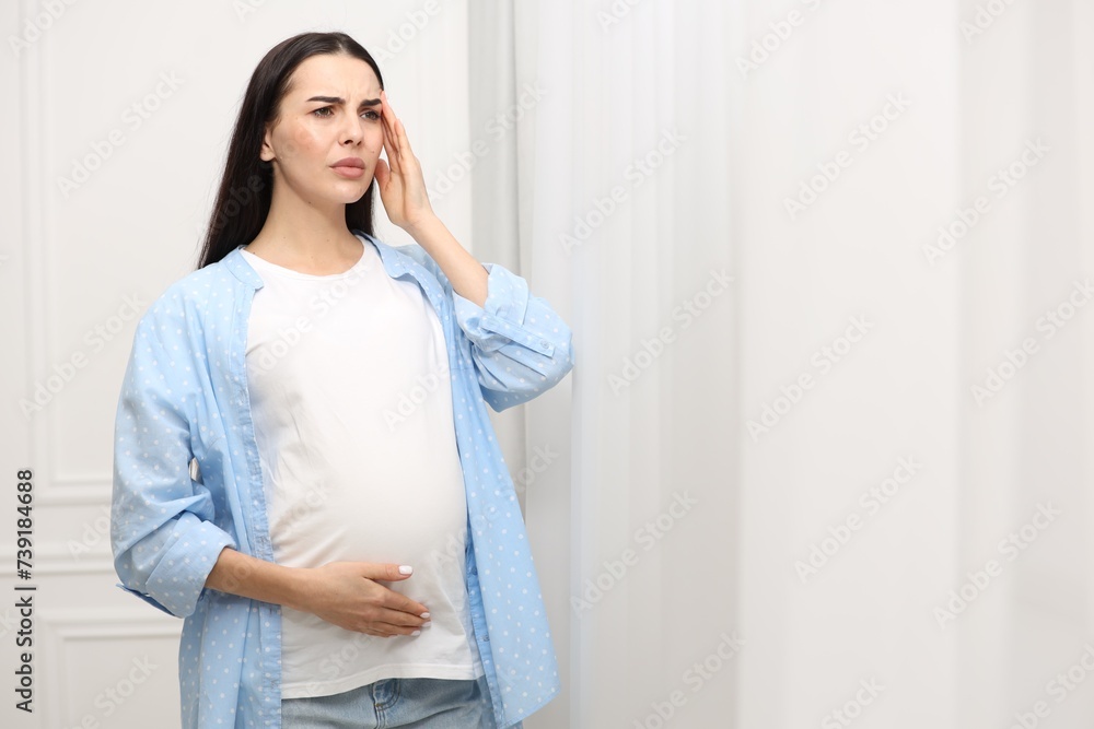 Pregnant woman suffering from headache indoors, space for text Pregnant woman suffering from headache indoors, space for text
