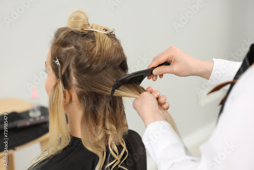 Hair styling. Professional hairdresser combing woman's hair indoors, closeup