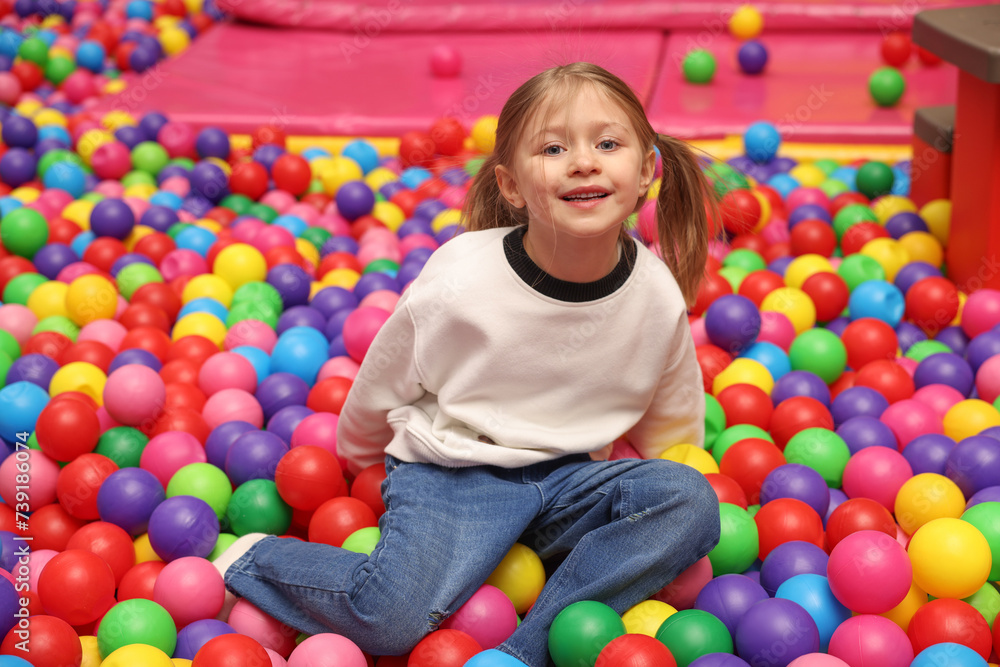 Obraz premium Happy little girl sitting on colorful balls in ball pit