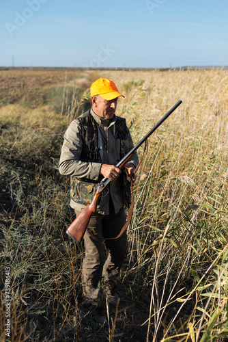 Mature man hunter with gun while walking on field.