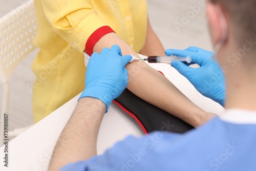 Doctor taking blood sample from patient with syringe at white table in hospital  closeup