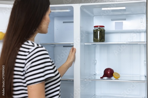 Young woman near empty refrigerator indoors, selective focus
