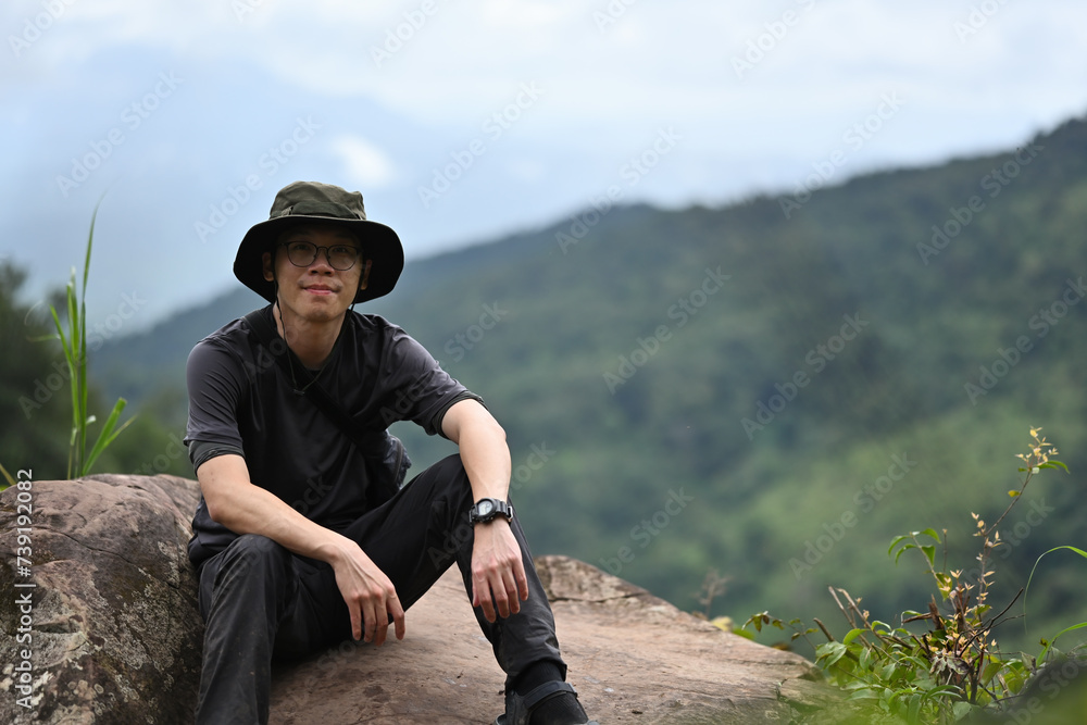 Young Asian male climber take a break at a rocky peak and the natural mountain landscape in the background, A Solo travel concept