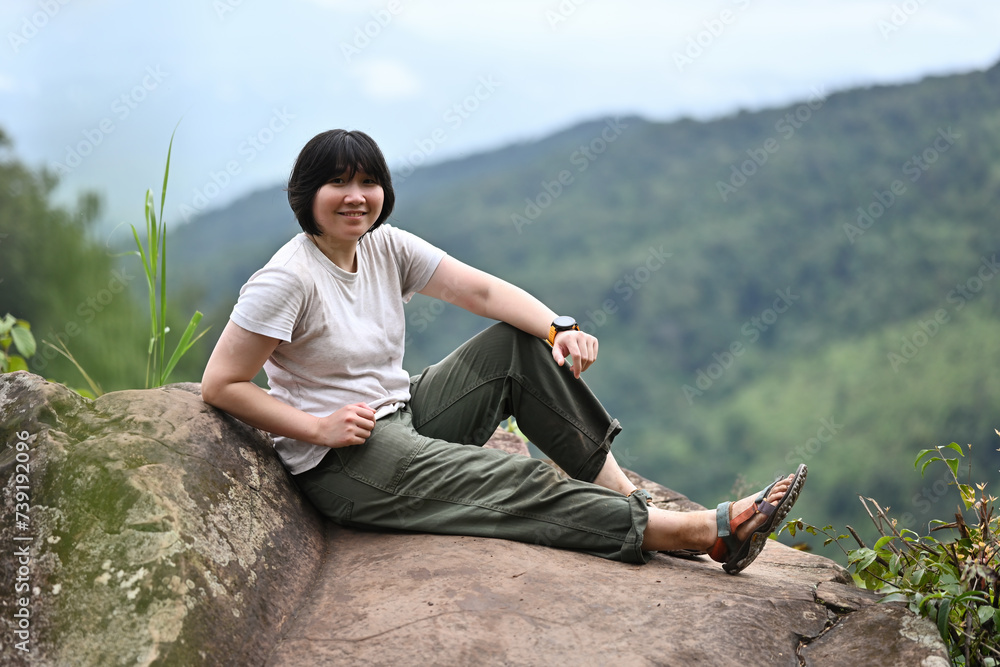 Asian female trail runner resting on rocks and natural mountain scenery in the background