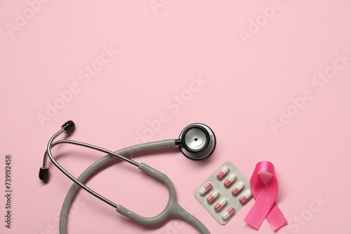 Breast cancer awareness. Pink ribbon, stethoscope and pills on color background, flat lay. Space for text