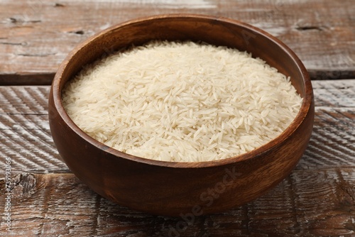 Raw basmati rice in bowl on wooden table, closeup