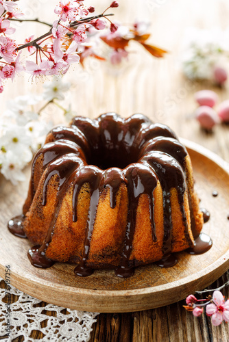 Chocolate and vanilla marble bundt cake, Babka with chocolate glaze on a plate on a wooden table decorated with spring flowers. Delicious easter dessert
