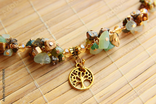 Delicate vintage bracelet made of a mix of natural stones jasper, jade with a golden tree of life pendant on a bamboo background.